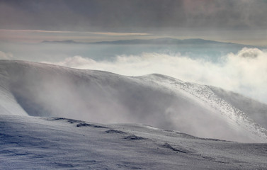 Windswept snowfields on ridges of Krizna peak in Velka Fatra with Vepor and Polana peaks of Slovak Central and Ore Mountains above low clouds and fog in winter dawn light, Carpathians Slovakia Europe