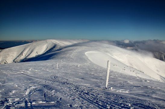 Ski tracks and wooden sticks in snow as trail sign to Ostredok highest peak of Velka Fatra in sunny snowfield on main ridge with low clouds and blue sky, Fatra Tatra Region Carpathians Slovakia Europe