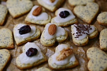 Valentine poppy seed sweet heart-shaped cookies topped with ice topping, hazelnuts, almonds and dried cranberries placed on baking paper