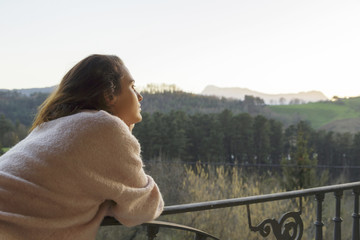 Pensive relaxed girl thinking on the balcony, looking at lonely. On an sunset landscape in Mallabia, Basque Country, Spain.