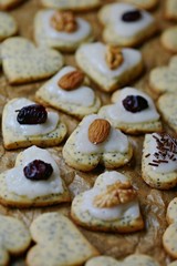 Vertical image of valentine poppy seed sweet heart-shaped cookies decorated with ice topping, hazelnuts, almonds and dried cranberries placed on baking paper