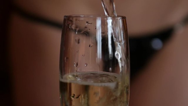 sexy young woman in a mini bikini pours champagne in glasses in a dark. close-up buttocks and hip