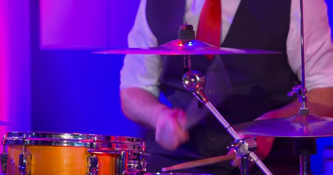 Close up of drummers hands as he keeps a steady beat on orange drim kit snare and cymbals