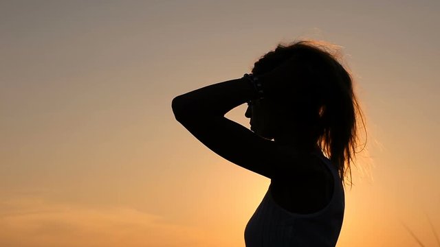 Silhouette of woman at sunset touches long hair- slow motion