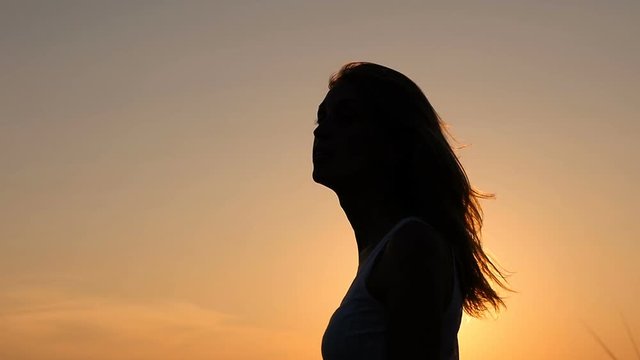 Silhouette of woman at sunset touches long hair- slow motion