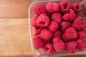 Fresh Raspberries in plastic container on wooden cutting board