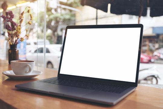 Mockup image of laptop with blank white desktop screen and coffee cup on wooden table in cafe