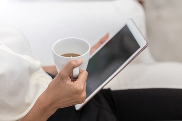 Woman holding coffee cup and tablet in hand