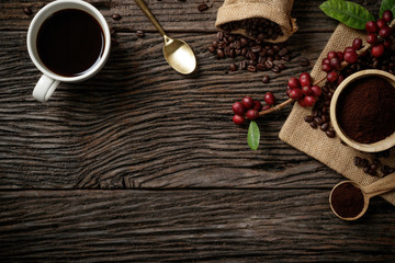 Top view mockup on wood background with a cup of coffee and red ripe coffee beans. Free space for...
