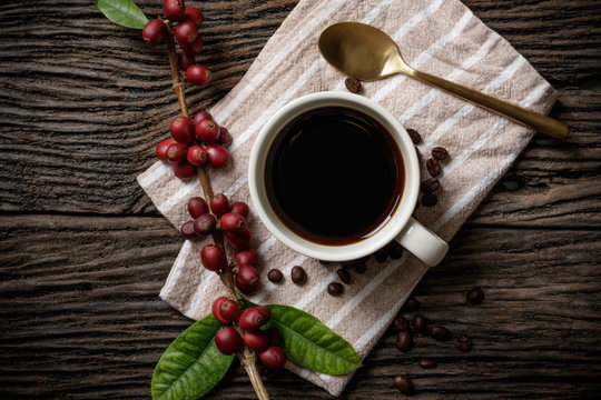 A cup of coffee on wooden desk with red ripe coffee beans.