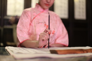 a woman in pink Chinese traditional costume with a Chinese writing brush in her hand, Chinese calligraphy