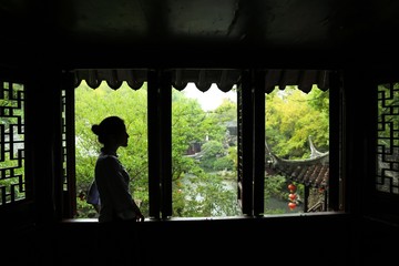 a woman in traditional Chinese costume standing at a traditional Chinese window, with traditional buildings as background
