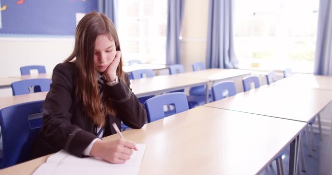 4K Young girl sitting alone & doing her work in school classroom, could be in detention or child with learning difficulties