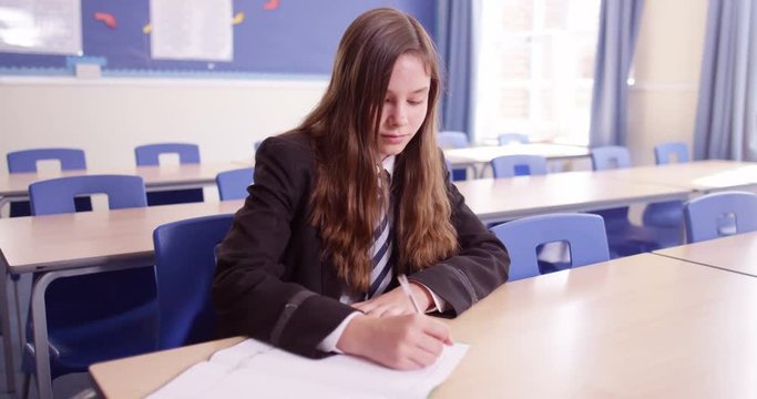 4K Young girl sitting alone & doing her work in school classroom, could be in detention or child with learning difficulties