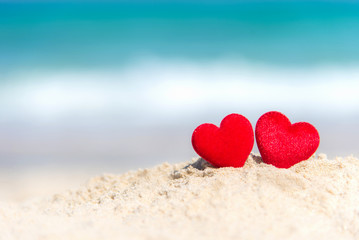 Valentine Concept.  Two red hearts on the sand summer beach, blue background.