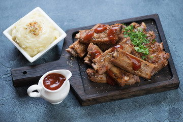 Black wooden serving tray with roasted pork ribs and mashed potato, studio shot, selective focus