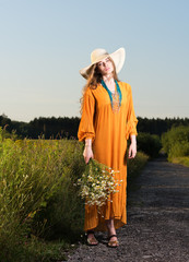 Summer look of a beautiful young woman in hat and red dress with a bouquet of daisies