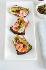 Smorrebrod, traditional Danish open sanwiches, dark rye bread with salmon, avocado, shrimp and micro-greenon a white plate. 
