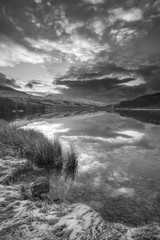 Stunning  black and white sunrise landscape image in Winter of Llyn Cwellyn in Snowdonia National Park with snow capped mountains in background
