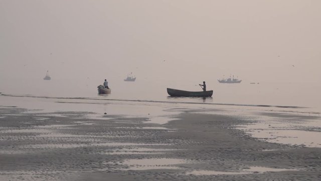 Fisherman paddles boat past beach covered in plastic garbage and other pollution in Mumbai, India 