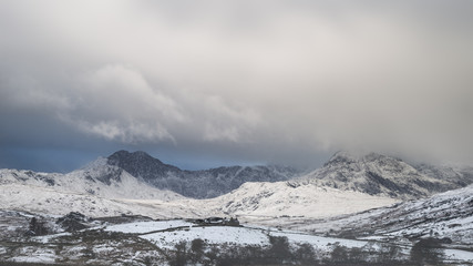 Beautiful Winter landscape image of Llynnau Mymbyr in Snowdonia National Park with snow capped mountains in background