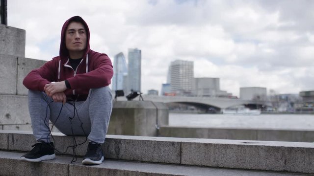Portrait of hooded male athlete sitting on steps in the city