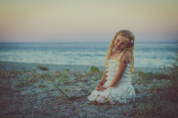 adorable girl with long blond hair sitting alone in the beach