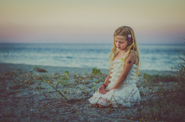 girl with long blond hair sitting alone  by the sea