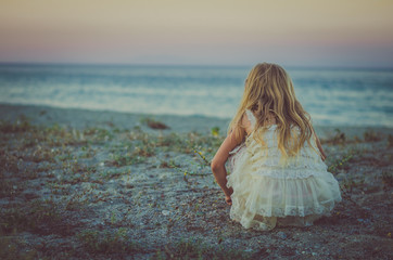 girl with long blond hair sitting alone in the beach back view