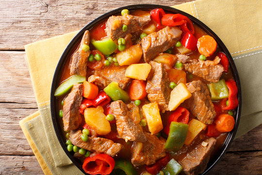 Slow cooked beef with potatoes, peppers, peas, tomatoes and carrots in a spicy sauce close-up. horizontal top view