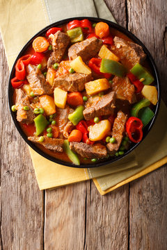 Asian food: Stewed beef with potatoes, peppers, peas, tomatoes and carrots close-up on the table. Vertical top view