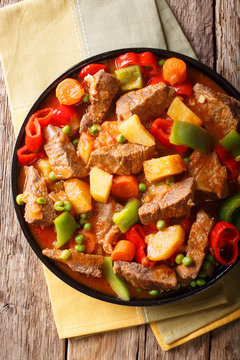Slow cooked beef with potatoes, peppers, peas, tomatoes and carrots in a spicy sauce close-up. Vertical top view