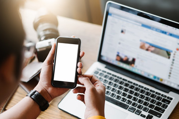 Mockup image of a man's hand holding white mobile phone with blank black desktop screen on thigh in cafe