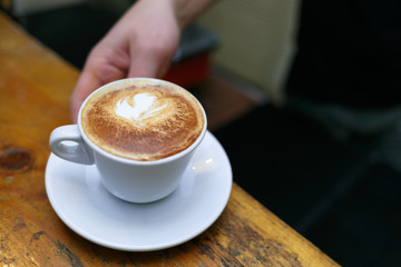 Hand barista holding and serving cup of coffee.