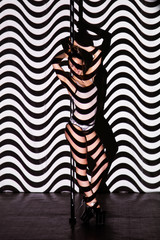 Fototapeta na wymiar Beautiful woman dances near a pole on a striped background.