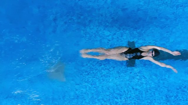 A swimmer moves on her back underwater before moving up. 