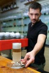 Men barista puts on bar a latte. Serving a client. Focus on beverage. Shallow depth of field.