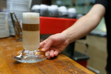Hand barista holding and serving glass of latte.