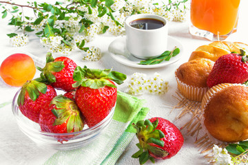 Breakfast from coffee, juice and strawberries and baked goods on a light background in a rustic style