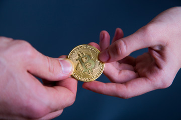 Person giving golden bitcoin to another person. Adult hands exchanging cryptocurrency.