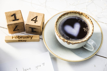 The heart is reflected in a cup of coffee on the table next to the wooden calendar. Valentine's Day Concept