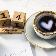 The heart is reflected in a cup of coffee on the table next to the wooden calendar. Valentine's Day Concept