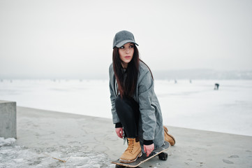 Stylish brunette girl in gray cap, casual street style with skate board on winter day.