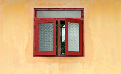 Fototapeta na wymiar Red window with shutters in yellow house facade