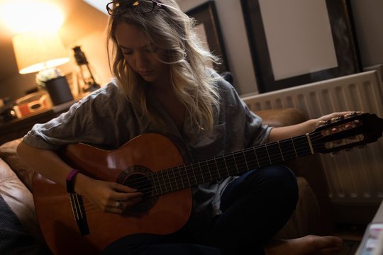 Young woman sitting and playing guitar 
