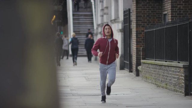 Young athletic male jogging on the street in daytime, in slow motion