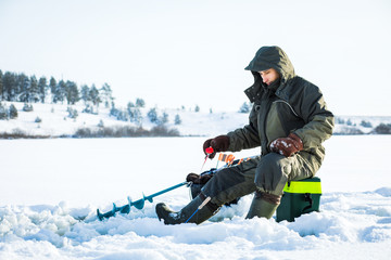 Fototapeta na wymiar A young man is fishing from a hole on ice. Winter fishing