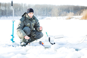 Fototapeta na wymiar A young man is fishing from a hole on ice. Winter fishing