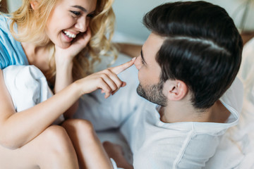 smiling girlfriend touching boyfriend nose in bed in morning