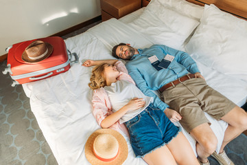 high angle view of couple of tourists lying on bed in hotel room - obrazy, fototapety, plakaty